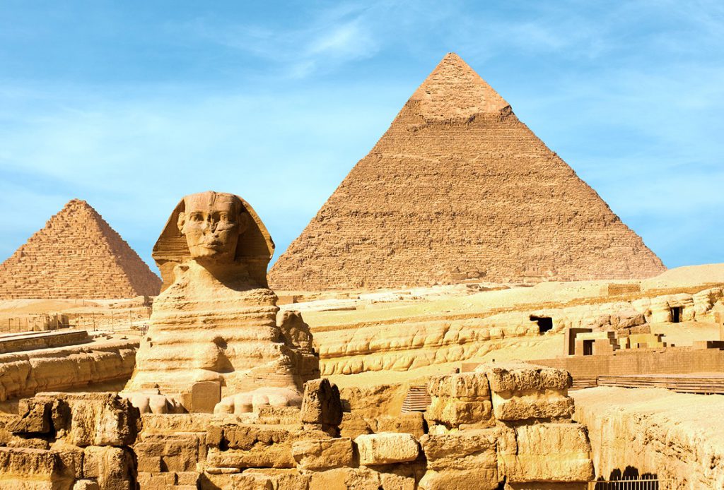 Sphinx and the large Egyptian Pyramids of Khafre, Menkaure slightly offset in front of blue sky in Giza, Cairo, Egypt. 