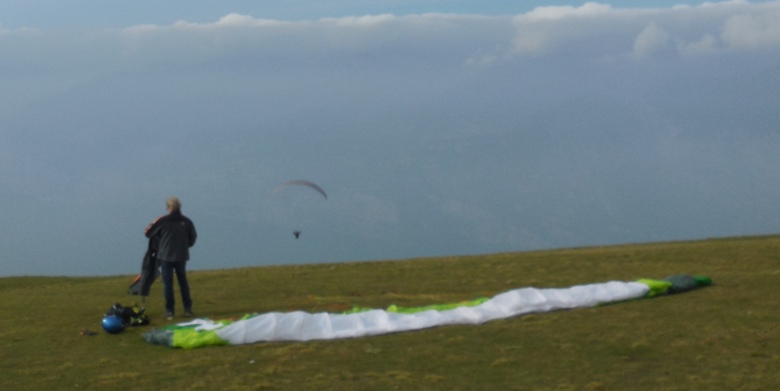 One paraglider airborne while another suits up on Monte Baldo overlooking Lake Garda