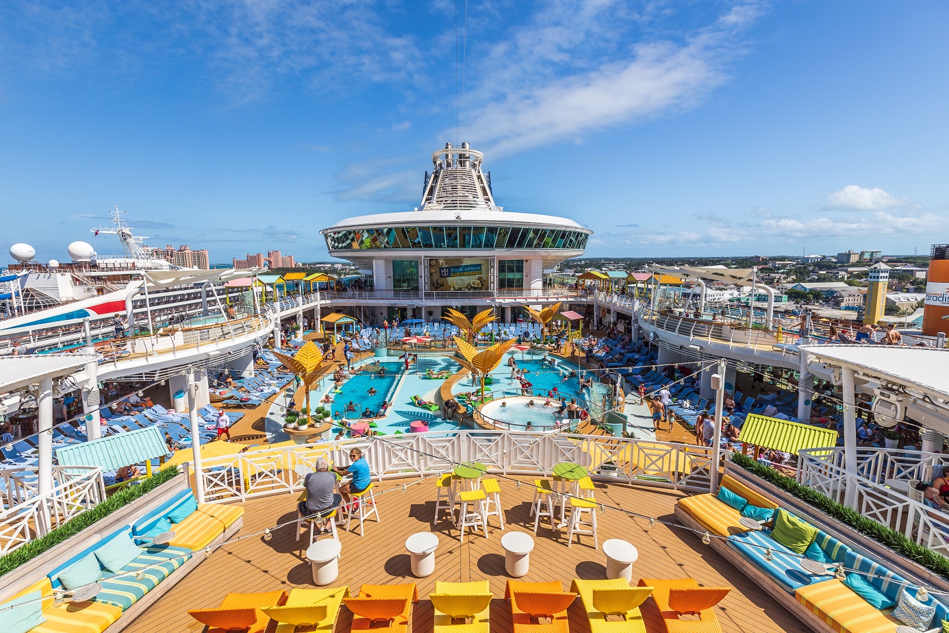 The top of a Royal Caribbean cruise ship with a balcony looking down over a pool with people and lounge chairs.