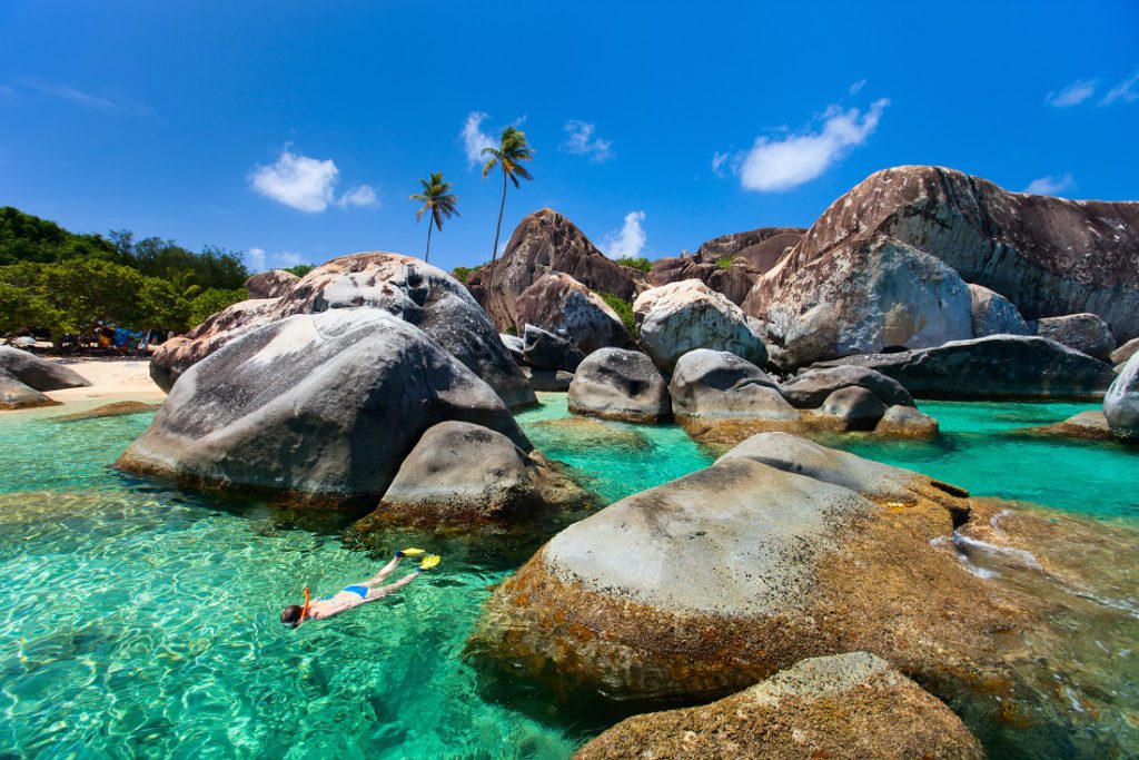 Young woman snorkeling in turquoise tropical water among huge granite boulders at The Baths beach area major tourist attraction on Virgin Gorda, British Virgin Islands, Caribbean