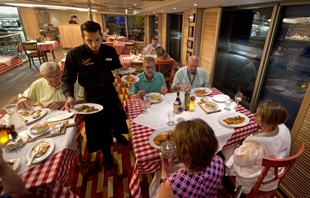 A server delivers entrées in Carnival Sunrises's Cucina del Capitano restaurant that offers delicious Italian favorites