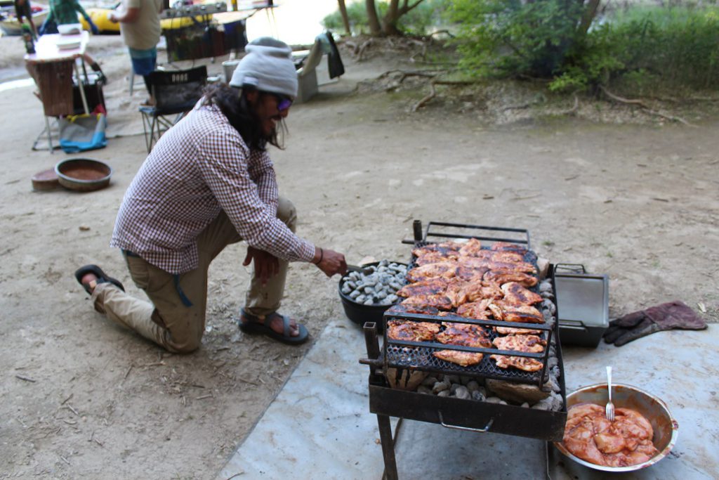 River guide Zach Sam cooking chicken over a bed of charcoal