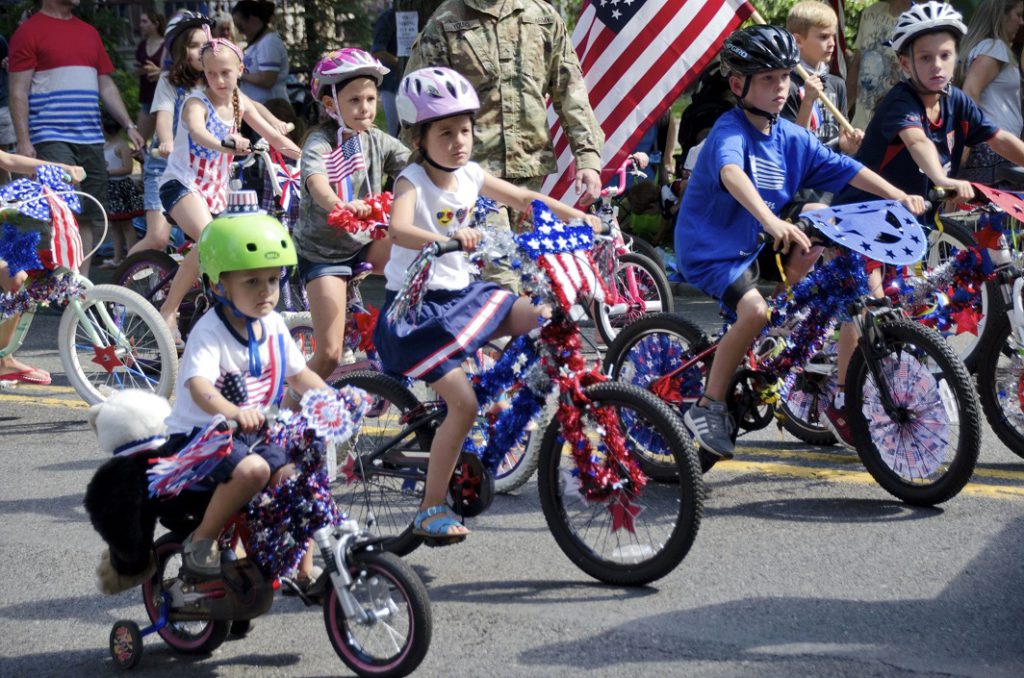 Children on decorated bicycles in a suburban Fourth of July Parade in a small suburban American town.