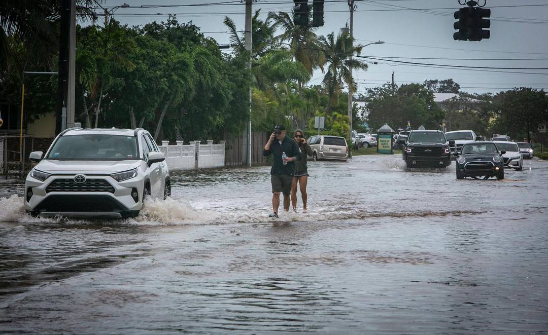 Key West, Florida, September 28, 2022 - People walk on the median surrounded by flood waters on Flagler Avenue in Key West. Hurricane Ian brushed Key West on its way to the mainland leaving flooded streets due to rain and storm surge.