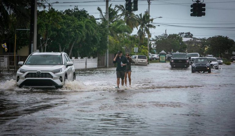 Key West, Florida, September 28, 2022 - People walk on the median surrounded by flood waters on Flagler Avenue in Key West. Hurricane Ian brushed Key West on its way to the mainland leaving flooded streets due to rain and storm surge.