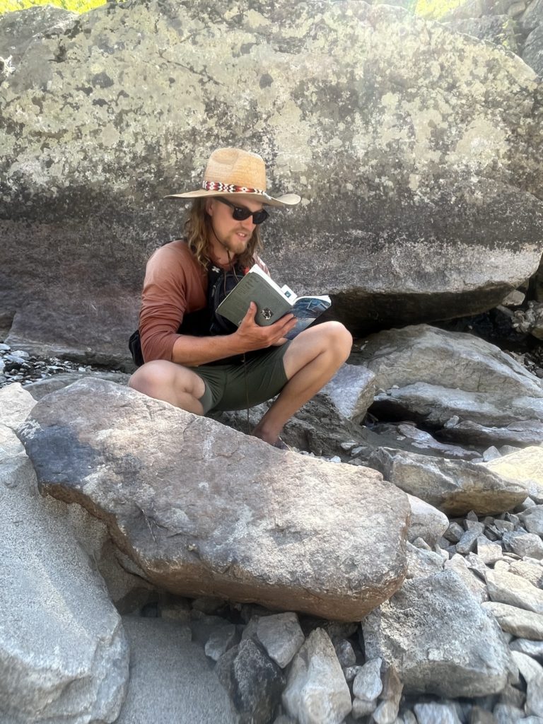 OARS Guide Ethan Nelson reads from a collection of short stories by river guides during a break from rowing one of the dories