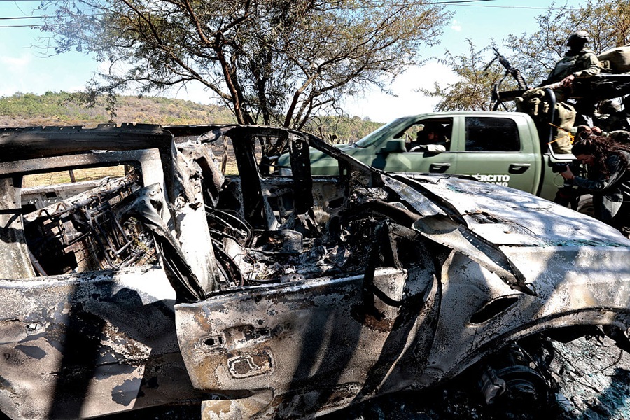 Members of the army onboard a truck are seen next to a burned car used to block roads while Mexican drug lord "El Mencho" tried to flee, near the "Tapalpa Country Club", where he was hiding at the moment of the operation in which he was killed, in Tapalpa, Jalisco state, Mexico, on February 24, 2026. Residents of Jalisco cautiously peeked their heads out on February 23, 2026 after waves of retaliatory cartel violence rocked the Mexican state over the weekend following the death of a major drug kingpin. (Photo by Ulises Ruiz / AFP via Getty Images)