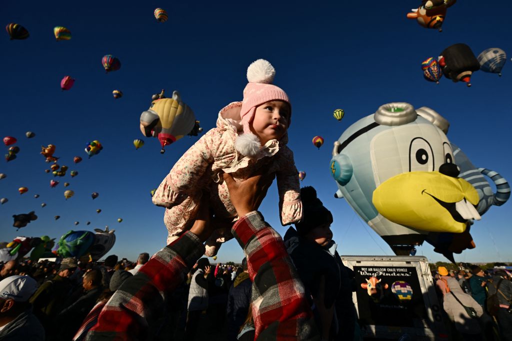TOPSHOT - Clarissa is lifted into the air by her father as hot air balloons take flight at sunrise during the Albuquerque International Balloon Fiesta in Albuquerque, New Mexico on October 13, 2023. (Photo by Patrick T. Fallon / AFP) (Photo by PATRICK T. FALLON/AFP via Getty Images)