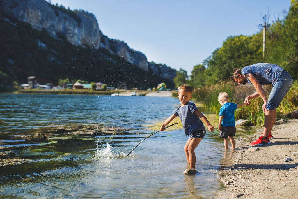 Children splashing in the lake with their father enjoying a warm sunny day outdoors.