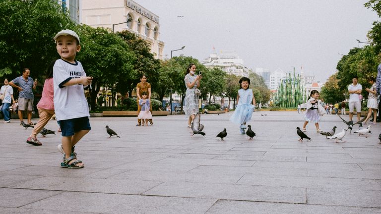 Joyful children play with pigeons in a lively city square, showcasing urban life.