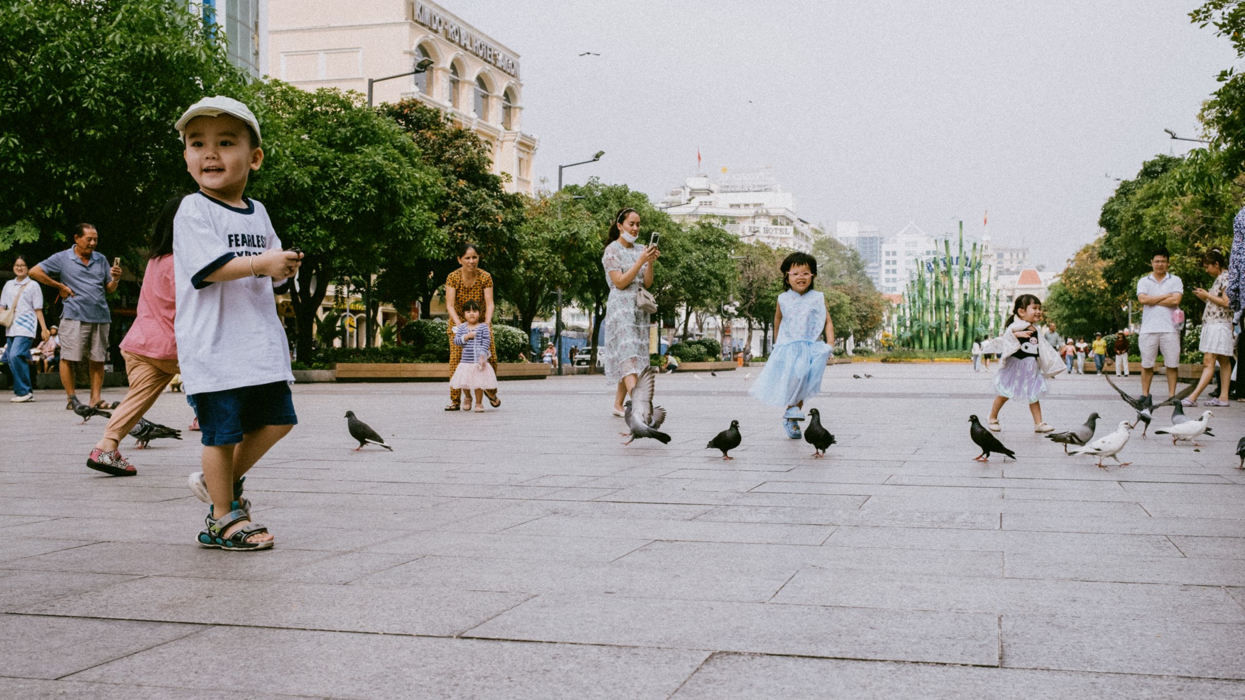 Joyful children play with pigeons in a lively city square, showcasing urban life.